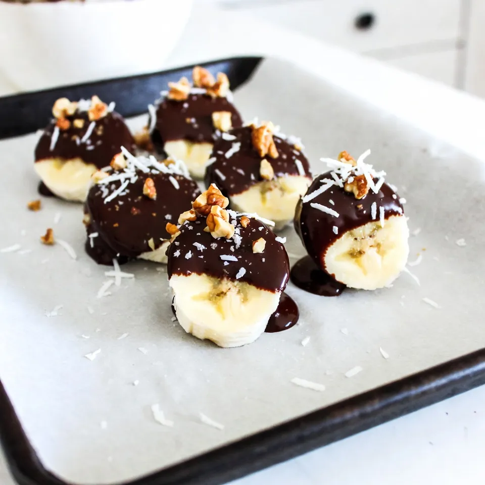 Für diese leckeren Snacks brauchst du nur wenige Zutaten. Hier ist, was du benötigst: - 2 reife Bananen - 1 Tasse Zartbitterschokoladenstückchen - 2 Esslöffel Kokosöl Mit diesen Hauptzutaten bereitest du die schokoladigen Bananenbisse zu. Die reifen Bananen geben eine süße Basis. Die Zartbitterschokolade sorgt für den schokoladigen Geschmack, während das Kokosöl die Schokolade schön geschmeidig macht. Um deinen Bananenbissen mehr Textur zu geben, kannst du einige gesunde Zusätze hinzufügen. Ich empfehle: - 1/4 Tasse gehackte Nüsse (Mandeln, Walnüsse oder Haselnüsse) - 1/4 Tasse ungesüßte Kokosraspeln - Meersalz, zum Bestreuen Diese Zutaten bringen nicht nur Crunch. Sie fügen auch gesunde Fette und Ballaststoffe hinzu. Die Nüsse bringen einen tollen Biss. Die Kokosraspeln geben ein tropisches Aroma. Ein Hauch von Meersalz hebt den Geschmack der Schokolade hervor. Schokolade ist der Schlüssel zu diesem Rezept. Wähle eine gute Qualität. Achte auf: - Zartbitterschokolade mit mindestens 70% Kakao - Bio- oder Fair-Trade-Schokolade für nachhaltige Optionen Hochwertige Schokolade hat einen reicheren Geschmack. Sie schmilzt auch besser. Das macht das Eintauchen der Bananen einfacher. Wenn du Milchschokolade magst, kannst du diese auch verwenden. Sie wird süßer sein, aber trotzdem lecker. {{ingredient_image_2}} Zuerst nimmst du zwei reife Bananen. Schäle sie und schneide sie in 2,5 cm dicke Scheiben. Lege die Bananenscheiben gleichmäßig auf ein mit Backpapier ausgelegtes Backblech. Jetzt ist es Zeit, die Bananen in das Gefrierfach zu stellen. Lass sie dort für etwa 30 Minuten. So werden sie fest und leicht zu handhaben. Während die Bananen gefrieren, kannst du die Schokolade vorbereiten. Nimm eine mikrowellengeeignete Schüssel. Füge 1 Tasse Zartbitterschokoladenstückchen und 2 Esslöffel Kokosöl hinzu. Stelle die Schüssel in die Mikrowelle. Erhitze die Mischung in 30-Sekunden-Intervallen. Rühre zwischendurch um, bis die Schokolade glatt und vollständig geschmolzen ist. Sobald die Bananenscheiben fest sind, nimm das Blech aus dem Gefrierfach. Jetzt tauchst du jede Bananenscheibe in die geschmolzene Schokolade. Verwende eine Gabel, um die Bananen gleichmäßig zu ummanteln. Lass überschüssige Schokolade abtropfen, bevor du die Scheiben zurück auf das Blech legst. Während die Schokolade noch feucht ist, streue die gehackten Nüsse und die Kokosraspeln darüber. Eine Prise Meersalz verleiht dem Ganzen den letzten Schliff. Stelle das Blech für 15-20 Minuten wieder ins Gefrierfach, bis die Schokolade hart ist. Voilà, deine schokoladenüberzogenen Bananenbisse sind fertig! Um perfekte Schokoladenüberzogene Bananenbisse zu machen, beachte diese Tipps: - Wähle reife, aber feste Bananen. Sie sind süß und leicht zu schneiden. - Gefriere die Bananenscheiben gut, damit sie beim Tauchen in die Schokolade nicht zerfallen. - Schmelze die Schokolade langsam. Benutze die Mikrowelle in kurzen Intervallen. - Tauche die Bananen vollständig in die Schokolade für einen tollen Geschmack. Es gibt einige häufige Fehler, die du vermeiden solltest: - Wenn du die Bananen nicht gefrierst, können sie matschig werden. - Verwende keine zu hohe Wärme zum Schmelzen der Schokolade. Sie kann anbrennen. - Lasse die Schokolade nicht zu lange stehen, bevor du die Toppings hinzufügst. Sie muss feucht sein, damit alles gut haftet. Du kannst deine Bananenbisse leicht anpassen: - Probiere verschiedene Nüsse wie Mandeln oder Walnüsse für neuen Crunch. - Füge Gewürze wie Zimt oder Chili für einen besonderen Kick hinzu. - Nutze verschiedene Schokoladen wie weiße oder Vollmilchschokolade für andere Geschmäcker. - Verwende getrocknete Früchte oder Müsli als Topping für mehr Textur. Pro Tipps Die richtige Banane wählen: Achte darauf, dass die Bananen reif, aber nicht überreif sind, um die beste Textur und Süße zu erzielen. Schokolade temperieren: Für einen schönen Glanz und eine bessere Konsistenz kannst du die Schokolade temperieren, bevor du die Bananen tauchst. Variationen ausprobieren: Experimentiere mit verschiedenen Nüssen oder füge Gewürze wie Zimt oder Vanille zu der Schokolade hinzu, um neue Geschmackskombinationen zu entdecken. Richtig lagern: Bewahre die Bananenbisse in einem luftdichten Behälter im Gefrierfach auf, um die Frische zu bewahren und ein Zusammenkleben zu verhindern. {{image_4}} Ich liebe es, mit verschiedenen Nüssen zu experimentieren. Du kannst Mandeln, Walnüsse oder Haselnüsse verwenden. Diese Nüsse geben den Bananenbissen einen tollen Crunch. Wenn du die Nüsse klein hackst, kannst du sie am besten auf die Bananenbisse streuen. Sie sorgen für einen schönen Kontrast zur weichen Banane und zur Schokolade. Kokosraspeln sind eine weitere leckere Option. Ich empfehle ungesüßte Kokosraspeln. Sie haben einen natürlichen Geschmack. Diese Raspeln geben den Bananenbissen eine besondere Note. Du kannst sie einfach auf die noch feuchte Schokolade streuen. Das sieht auch toll aus! Du kannst deinem Rezept auch andere Aromen hinzufügen. Zum Beispiel: - Zimt: Ein Hauch Zimt macht alles besser. - Erdnussbutter: Ein Klecks Erdnussbutter gibt einen tollen Geschmack. - Honig: Ein wenig Honig bringt Süße in die Mischung. Alle diese Ideen machen deine Bananenbisse einzigartig. Experimentiere und finde deine Lieblingsversion! Schokoladenüberzogene Bananenbisse sind im Gefrierfach bis zu zwei Monate haltbar. Die Bananen bleiben frisch und lecker, wenn du sie richtig lagerst. Achte darauf, dass sie in einem luftdichten Behälter sind. So schütze ich sie vor Frostbrand und vermeide, dass sie ihren Geschmack verlieren. Die besten Lagerbedingungen für deine Bananenbisse sind im Gefrierfach. Ich empfehle, die Bananenbisse auf ein Backblech zu legen und einzufrieren. Nach dem Aushärten kannst du sie in einen Behälter umfüllen. So bleiben sie fest und klumpen nicht zusammen. Halte die Temperatur konstant bei -18 °C oder kälter. Um die Bananenbisse richtig einzufrieren, folge diesen Schritten: - Schneide die Bananen in dicke Scheiben. - Lege sie zuerst auf ein Backblech. - Friere sie für 30 Minuten ein, bis sie fest sind. - Tauche sie in Schokolade und dekoriere sie. - Lass sie erneut 15-20 Minuten gefrieren, bis die Schokolade fest ist. - Fülle die Bananenbisse in einen luftdichten Behälter. So bleiben die Bananenbisse knackig und köstlich. Um Schokoladenüberzogene Bananenbisse zu machen, folge diesen Schritten: 1. Bananen vorbereiten: Schäle zwei reife Bananen und schneide sie in 2,5 cm dicke Scheiben. 2. Bananen einfrieren: Lege die Scheiben auf ein mit Backpapier ausgelegtes Blech. Stelle das Blech für 30 Minuten ins Gefrierfach. 3. Schokolade schmelzen: Vermenge 1 Tasse Zartbitterschokoladenstückchen mit 2 Esslöffeln Kokosöl. Erhitze die Mischung in der Mikrowelle in 30-Sekunden-Intervallen. 4. Bananen tauchen: Nimm die gefrorenen Bananenscheiben. Tauche jede Scheibe in die geschmolzene Schokolade und lasse den Überschuss abtropfen. 5. Dekorieren: Streue gehackte Nüsse und Kokosraspeln auf die noch feuchte Schokolade. 6. Fertigstellen: Stelle das Blech wieder ins Gefrierfach für 15-20 Minuten, bis die Schokolade hart ist. Für Schokoladenüberzogene Bananenbisse sind Mandeln, Walnüsse oder Haselnüsse am besten geeignet. Diese Nüsse bringen einen tollen Crunch und Geschmack. Du kannst die Nüsse grob hacken und sie nach Belieben in die Schokolade streuen. Ja, du kannst auch andere Fette verwenden. Butter oder pflanzliches Öl sind gute Alternativen zu Kokosöl. Sie helfen der Schokolade, glatt zu werden und erleichtern das Eintauchen der Bananen. Achte darauf, dass das Fett einen neutralen Geschmack hat, um den Schokoladengeschmack nicht zu überdecken. Bananenbisse in Schokolade sind einfach zuzubereiten und schmecken köstlich. Wir haben die Hauptzutaten betrachtet und wie man sie kombiniert. Die Schritt-für-Schritt-Anleitung sorgt für Erfolg. Mit unseren Tipps vermeidest du Fehler und findest kreative Variationen. Wenn du die Bananenbisse richtig lagerst, bleiben sie frisch. Nutze diese Informationen, um leckere Snacks zu kreieren, die jeder liebt. Damit kannst du jede Gelegenheit versüßen. Viel Spaß beim Ausprobieren!